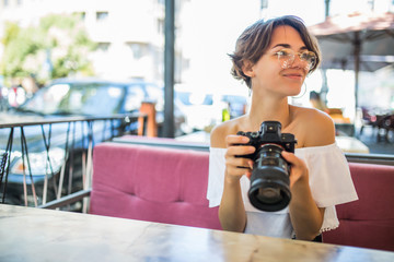 Young smiling woman look at pictures with a camera on the background of outdoor cafe