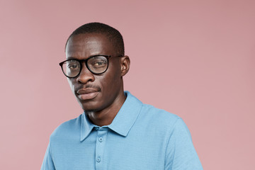 Portrait of African handsome guy in eyeglasses and in casual clothing looking at camera over pink...