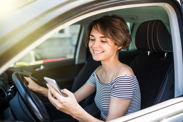 Young woman driver sitting behind the steering wheel reading a text message on a mobile