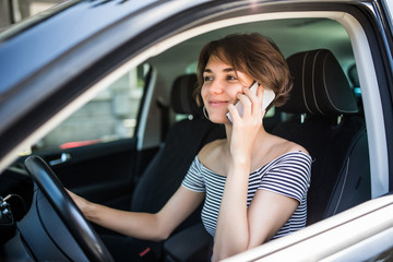 Young pretty woman with telephone having phone conversation while driving car