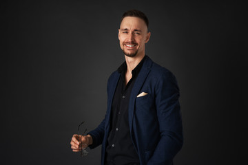 Studio portrait of a young successful guy with a mustache and a beard in a jacket on a dark background.