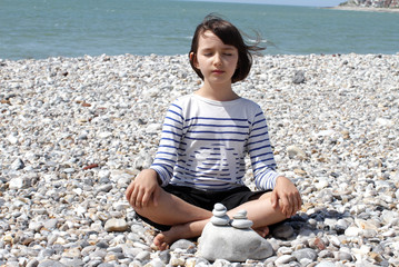 Fototapeta na wymiar calm child sitting with zen pebbles for mindfulness, water foreground