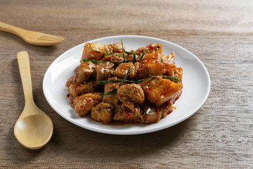 close up of stir fried pork belly with red curry paste in a ceramic dish on wooden table. hot and spicy thai style food menu.