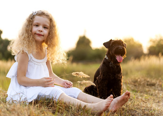 little girl with a dog plays in the park at sunset