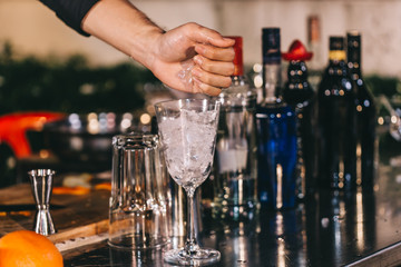 Bartender`s hands sprinkling the juice into the cocktail glass filled with alcoholic drink and making a smoky note on the dark background
