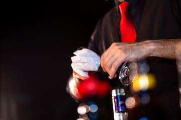 Bartender`s hands sprinkling the juice into the cocktail glass filled with alcoholic drink and making a smoky note on the dark background