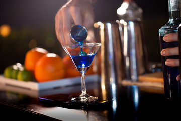 Bartenders hands sprinkling the juice into the cocktail glass filled with alcoholic drink and making a smoky note on the dark background