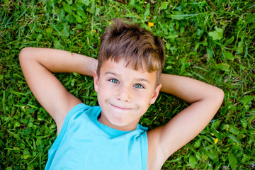 Portrait of little boy in blue t-shirt with green eyes lying on the grass