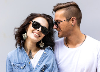 fashion couple in sunglasses posing on gray wall