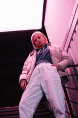 low angle view of stylish blonde woman in down jacket with hand in pocket looking at camera