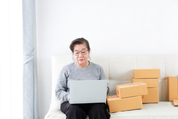 Asian senior woman retirement using laptop computer and packing box selling online market concept