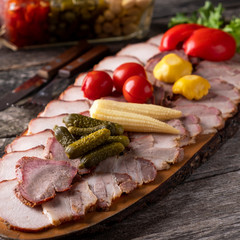 Assorted of smoked meat with marinated vegetables on wooden board.