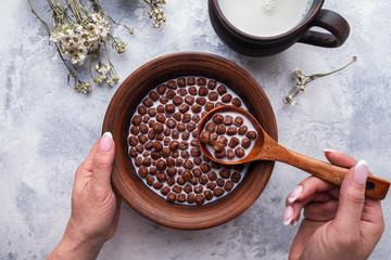 Hand holding spoon with chocolate cereal balls. Healthy breakfast and diet concept. Top view.