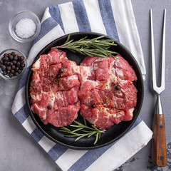 Slices of raw pork neck with spices on frying pan. Top view. Closeup