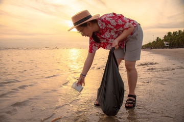 Asian women tourists picking up plastic garbage cleaning on the beach During the sunset . Tourists...