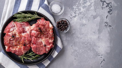 Slices of raw pork neck with spices on frying pan. Copy space. Top view