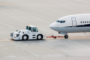 airplane on airport runway with pushback tractor.