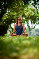 Smiling Caucasian woman in sports clothing sitting on mat in nature and meditating.