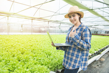 Obraz premium Portrait of happiness asian woman farmer or gardener with hand hold laptop in greenhouse hydroponic organic farm .Small business entrepreneur and organic vegetable farm and healthy food concept