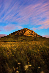 Mount Toratau against a starry sky and field with flowers in the foreground. Night photograph of stars and mountains. Clouds at night