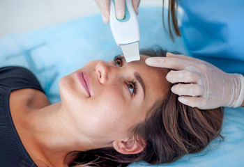 Naklejka premium cosmetologist with a patient during facial procedures in a modern cosmetological and aesthetic clinic. A patient receives an electric facial massage. Skin rejuvenation and wrinkle smoothing.