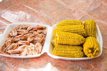 A tray is filled with corn and shrimp. Picnic outdoor