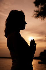 Silhouette of woman standing in praying position at sunset. Yoga exercising concept.