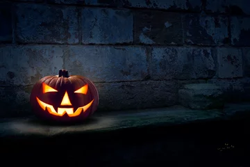 Foto auf Acrylglas A single scary evil looking halloween Jack O Lantern on the left side of a dark blue stone plinth background of a haunted castle at night. © Duncan Andison