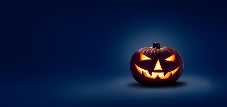 A halloween lit Jack O Lantern in a spotlight glow on a wide dark blue background
