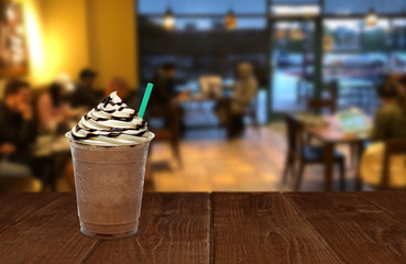 Iced coffee or frappuccino in plastic takeaway or to go cup on wooden table at cafe and people
