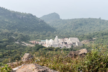 Fototapeta na wymiar White pagoda style Jain Temples surrounded by Parasnath Hill Range, trees, and jungles in forested area. Scenic Landscape View of holiest Jain Teerths. A Jharkhand tourism photography.