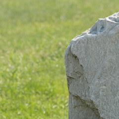 Parts of a huge grey stone from the side isolated from a green grassland. There is copy space in the background.