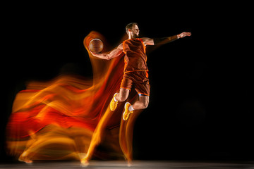 The fire tracks. Young caucasian basketball player of red team in action and jump in mixed light...