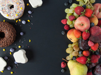 A lot of natural and healthy vitamin fruits, berries vs sweet and junk food on a black background....