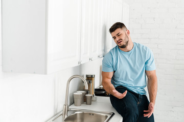 selective focus of upset man looking at faucet and sink in kitchen