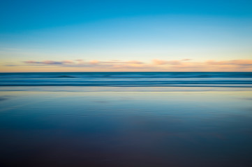 Scenic view of the glassy smooth shore of a deserted beach during the magic hour of sunset
