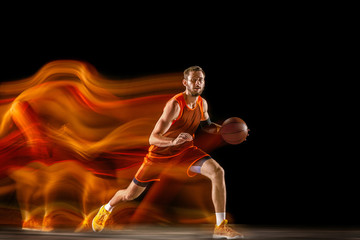 Becoming a winner. Young caucasian basketball player of red team in action and jump in mixed light over dark studio background. Concept of sport, movement, energy and dynamic, healthy lifestyle.
