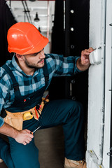 handsome bearded worker in safety helmet touching light switch