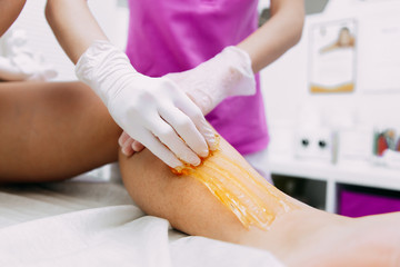 Obraz na płótnie Canvas Beautician depilating young woman's legs with liquid sugar in spa center.