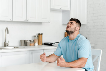 angry man gesturing while sitting near table in kitchen