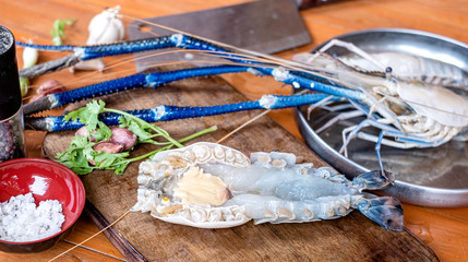 Raw whole and peeled big prawn with herbs on wooden cutting board with knife and scissors.