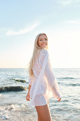 Fototapeta na wymiar Young joyful blond woman in white shirt happily looking aside with sea on background