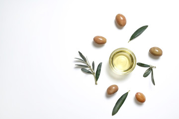 Bunch of local produce Turkish green gemlik olives with glass cup of extra virgin golden oil and olea europaea tree leaves. Close up, top view, copy space, isolated white background.