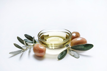 Bunch of local produce Turkish green gemlik olives with glass cup of extra virgin golden oil and olea europaea tree leaves. Close up, top view, copy space, isolated white background.