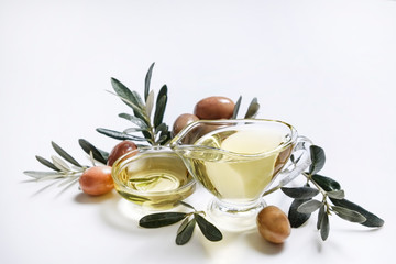 Bunch of local produce Turkish green gemlik olives with glass cup & gravy boat full of extra virgin golden oil, olea europaea tree leaves. Close up, top view, copy space, isolated white background.