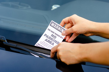 Close-up Of A Woman Taking Parking Ticket On Car's Windshield