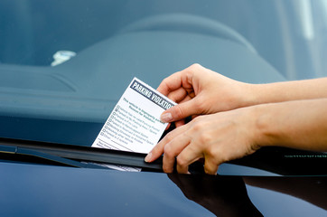 Close-up Of A Woman Taking Parking Ticket On Car's Windshield