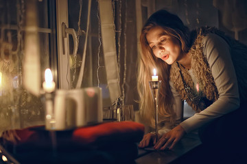 Christmas evening girl / beautiful young adult model, dreams and makes wishes at the candles in the New Year's Eve