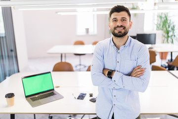 Portrait of attractive young man standing with crossed arms in modern office