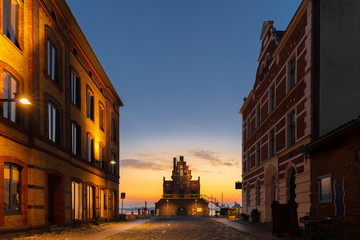 Fototapeta na wymiar In the morning just before sunrise at the harbor of the German city Stralsund on the Baltic Sea. The lanterns are still lit and the sky is orange and blue.